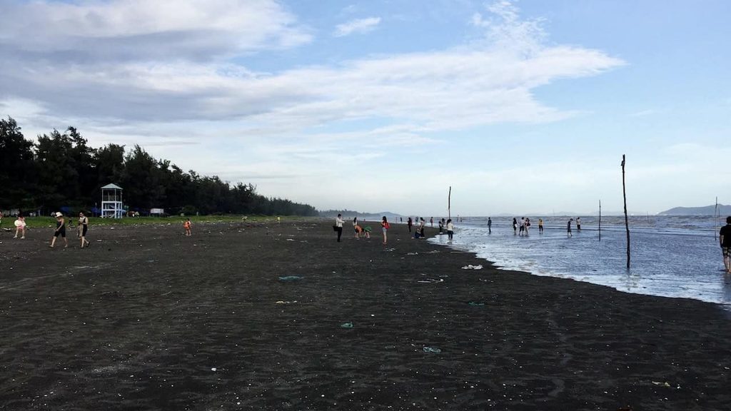 Visitors enjoying the black sand shoreline at 30/4 Beach in Can Gio