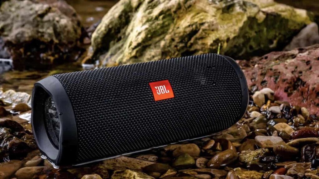 Black JBL portable Bluetooth speaker resting on wet rocks beside a stream