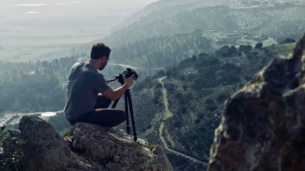 Traveler setting up a camera on a tripod overlooking a scenic mountain valley