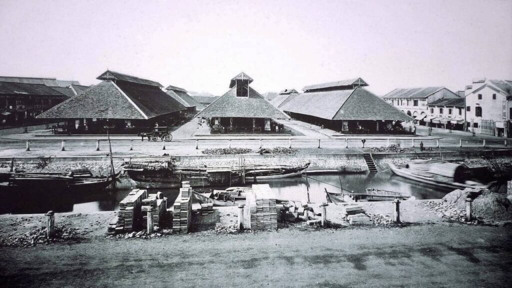 Historic black-and-white photograph of an early Ben Thanh Market in Saigon with traditional market buildings, boats, and a canal.