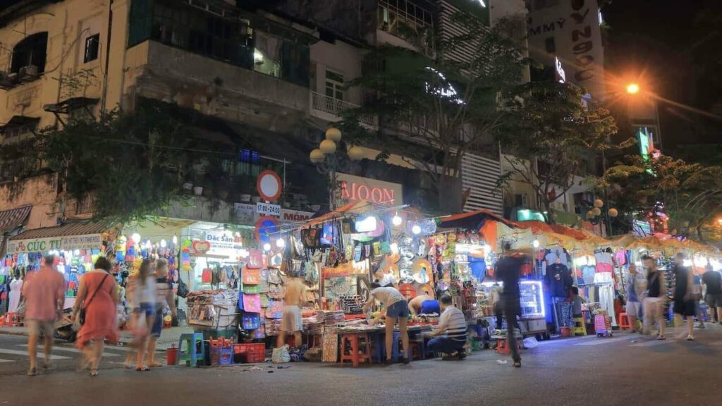 Ben Thanh Night Market in Ho Chi Minh City filled with colorful stalls, clothing, souvenirs, food vendors, and evening shoppers.