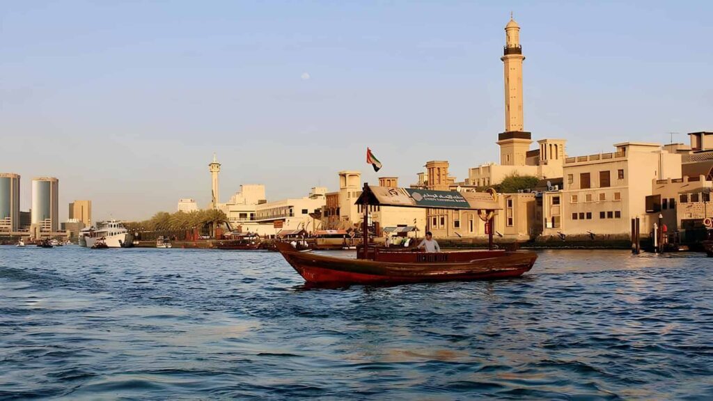 Traditional wooden abra boat crossing Dubai Creek beside historic waterfront buildings