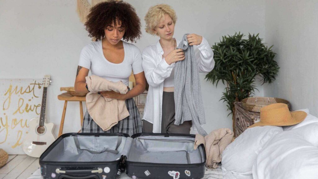 two girls are folding clothes to put in a luggage