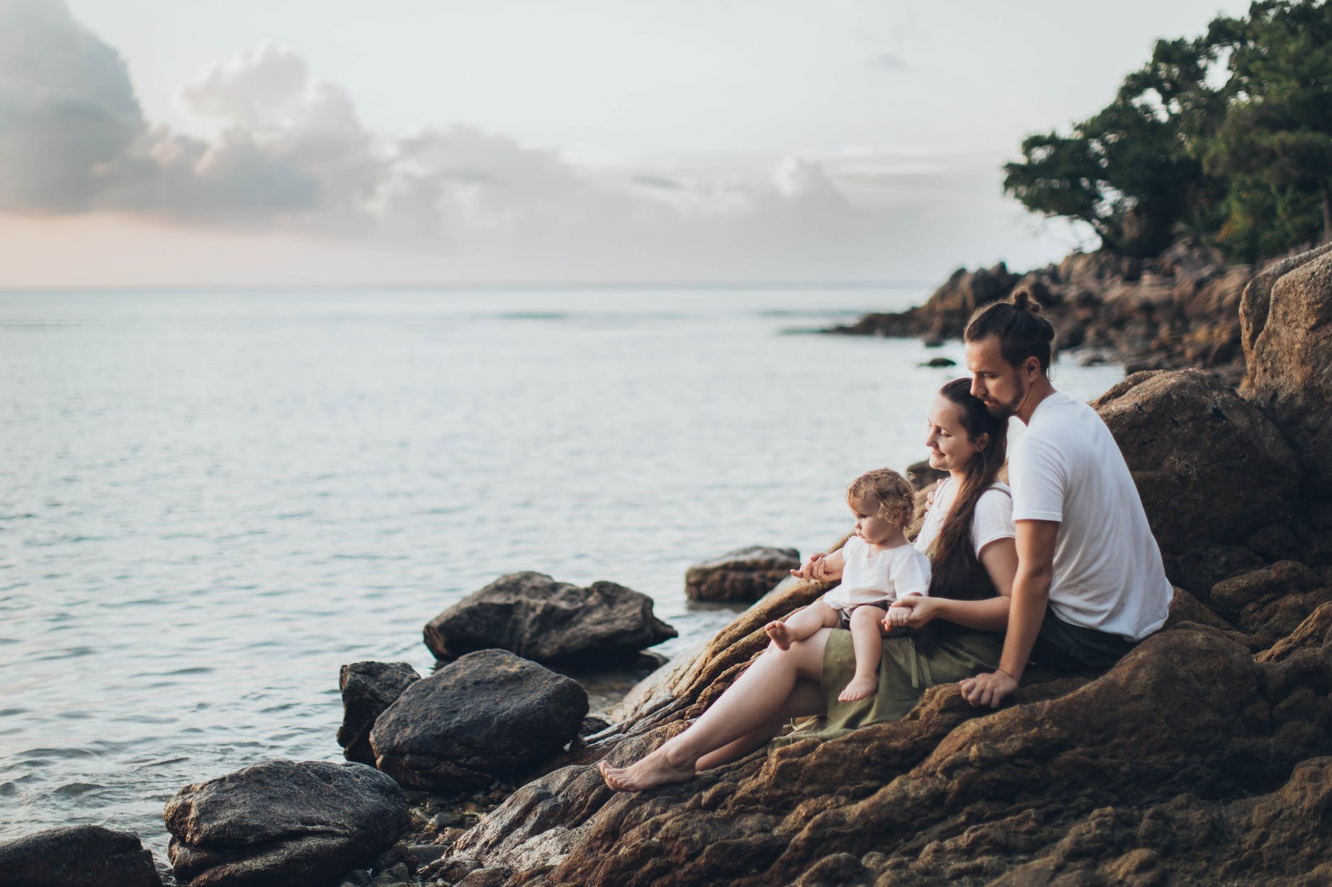 family of 3 sitting on rock near seashore