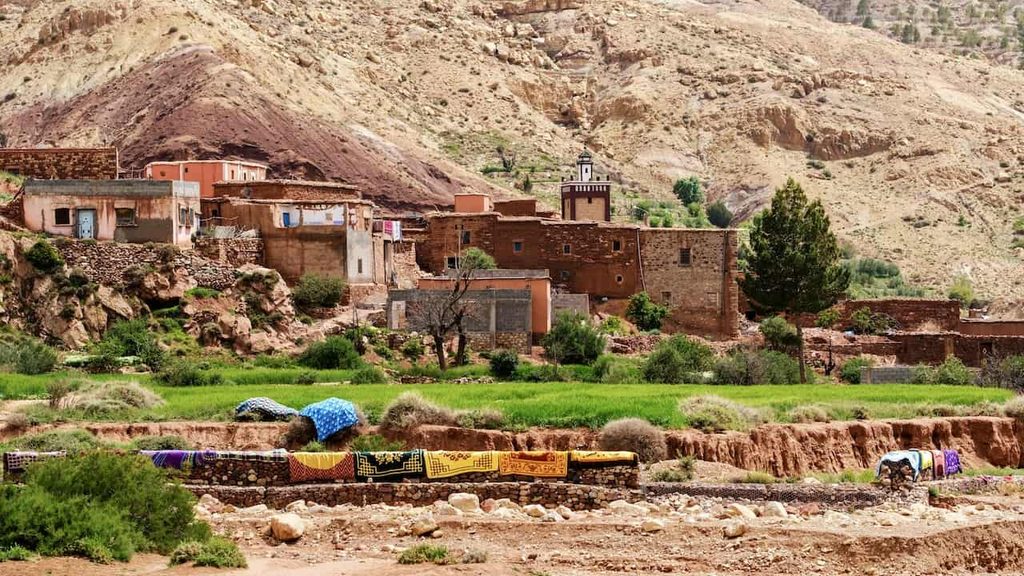 Traditional Berber village surrounded by green fields and rugged Atlas Mountains in Morocco