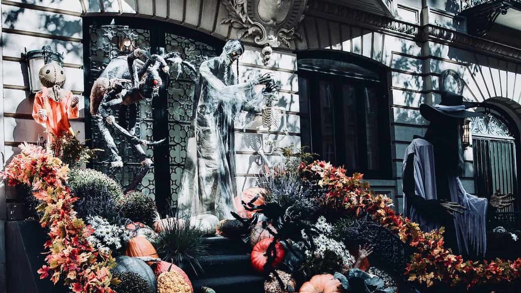 Elaborate Halloween decorations featuring skeletons, pumpkins, autumn flowers, and spooky figures outside a building.