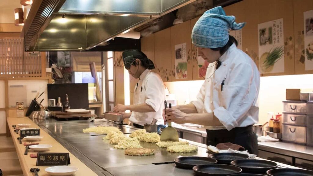 Chefs preparing Okonomiyaki on a traditional Japanese teppan griddle