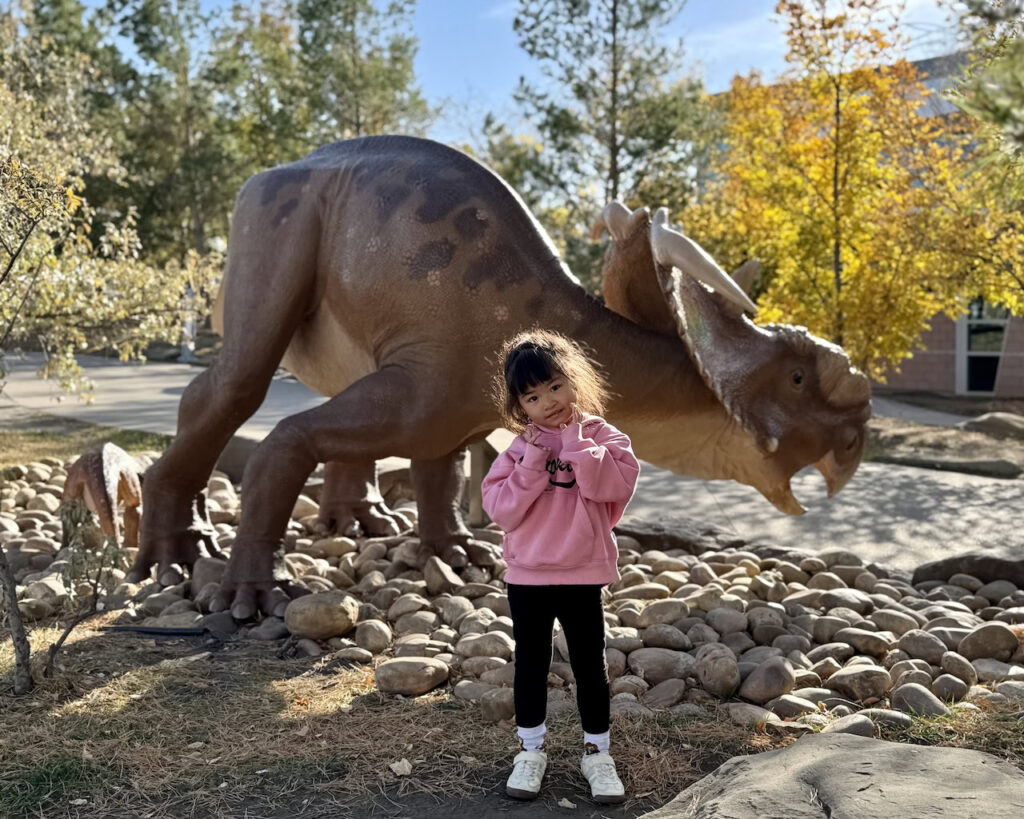 Child posing with outdoor dinosaur sculpture at the Royal Tyrrell Museum