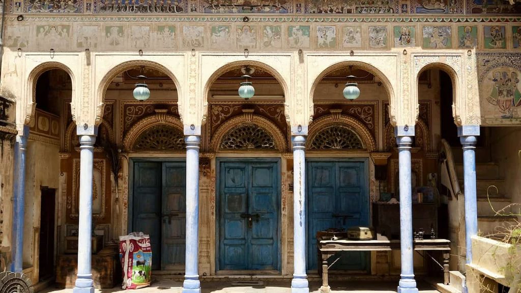 Traditional haveli facade with colorful frescoes, ornate arches, and blue wooden doors in Rajasthan, India